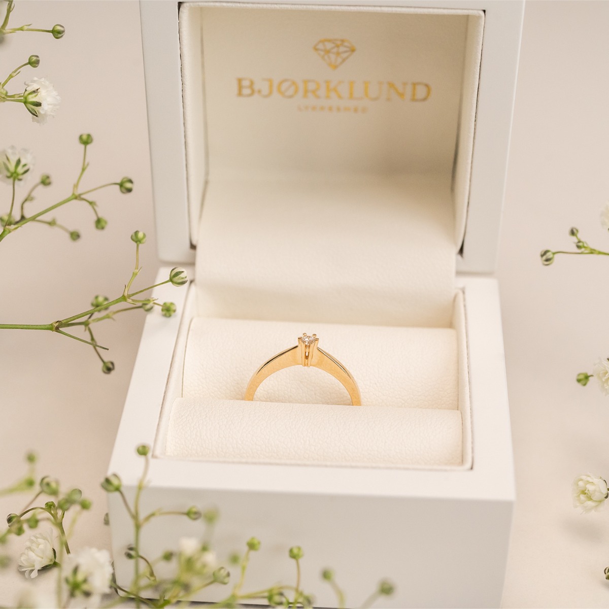 En enkel ring med glatt overflate og en liten, rund klartslip diamant festet i en seksklør-fatning midt på ringen.