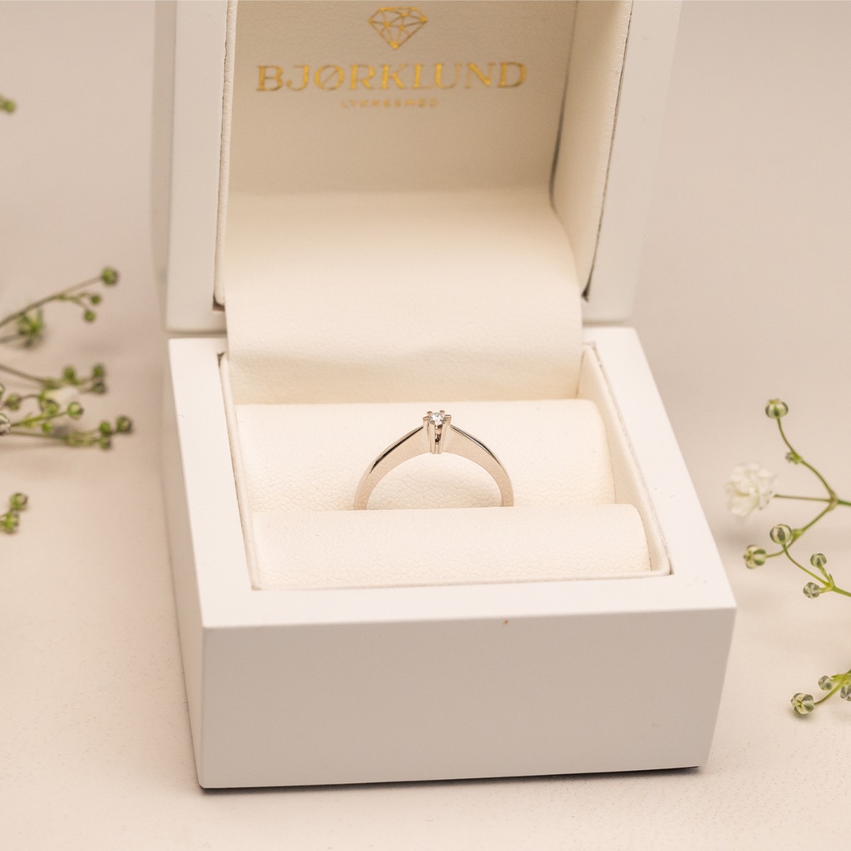 Enkel ring med liten, klartslip diamant festet i seksklør-fatning, vist på hvit bakgrunn med blank overflate.