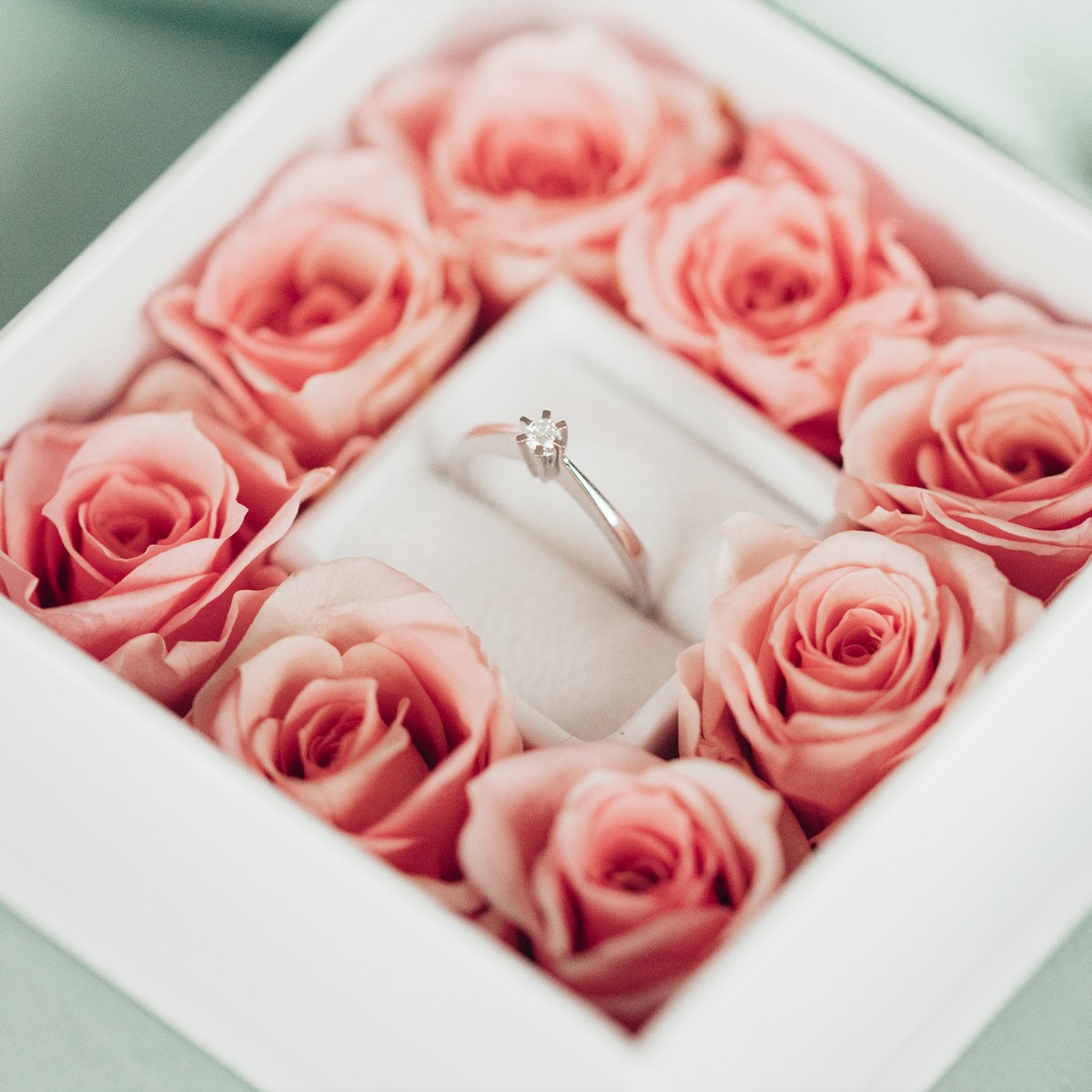 Ring i hvitt metall med en rund, klar sten i firkløft-fatning. Ringen har en smal, glatt skinnegang med lette facetter og vises ovenfra.