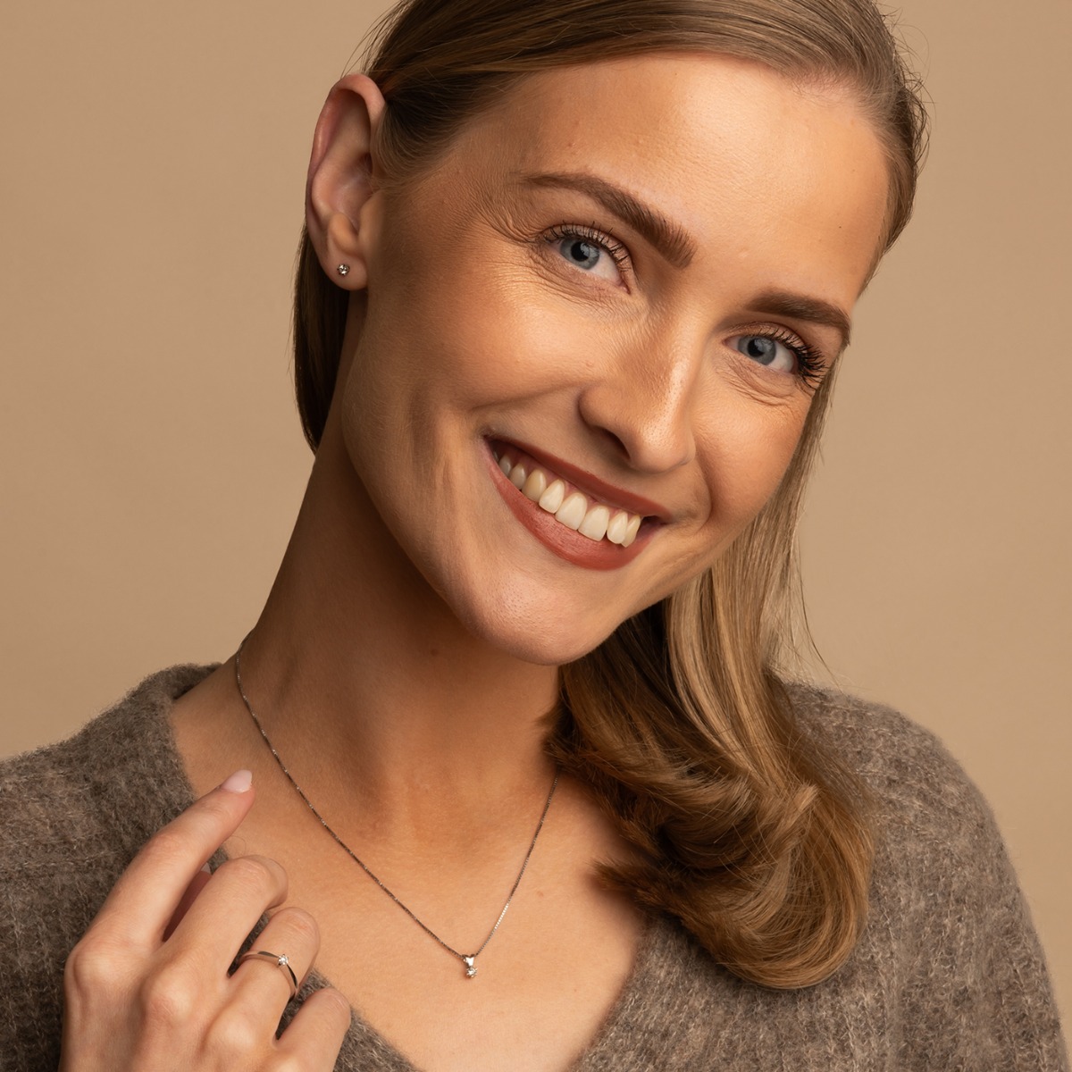 Kjede i lyst metall med firkantmønster og et lite anheng med rund, klar stein mot hvit bakgrunn.