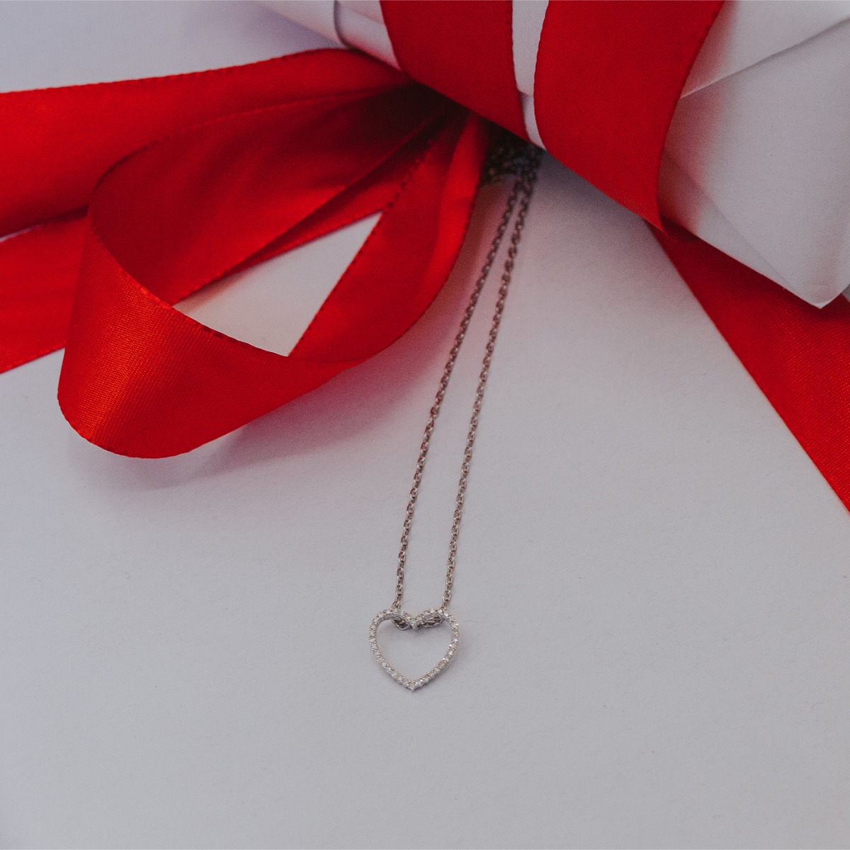 Halskjede i hvitt gull med åpent hjerteanheng besatt med små diamanter, avbildet mot hvit bakgrunn.