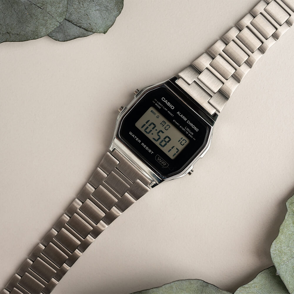 Sølvfarget digital armbåndsur med rektangulær skjerm som viser klokkeslettet 10:58:50 og tekst om alarm og vannmotstand.