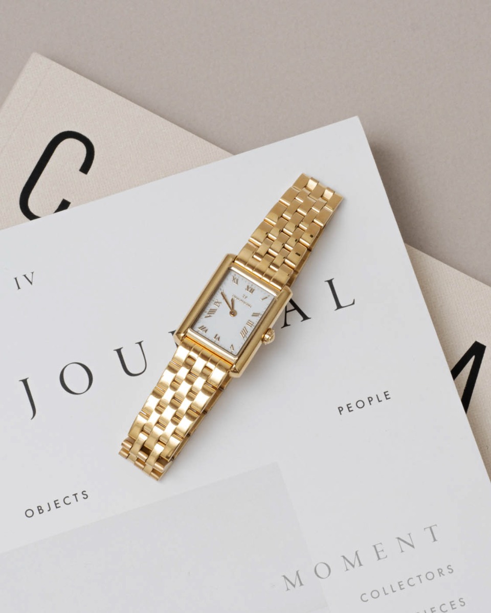 Rektangulær gullfarget armbåndsur med hvit urskive og romertall, festet til lenke i polert metall