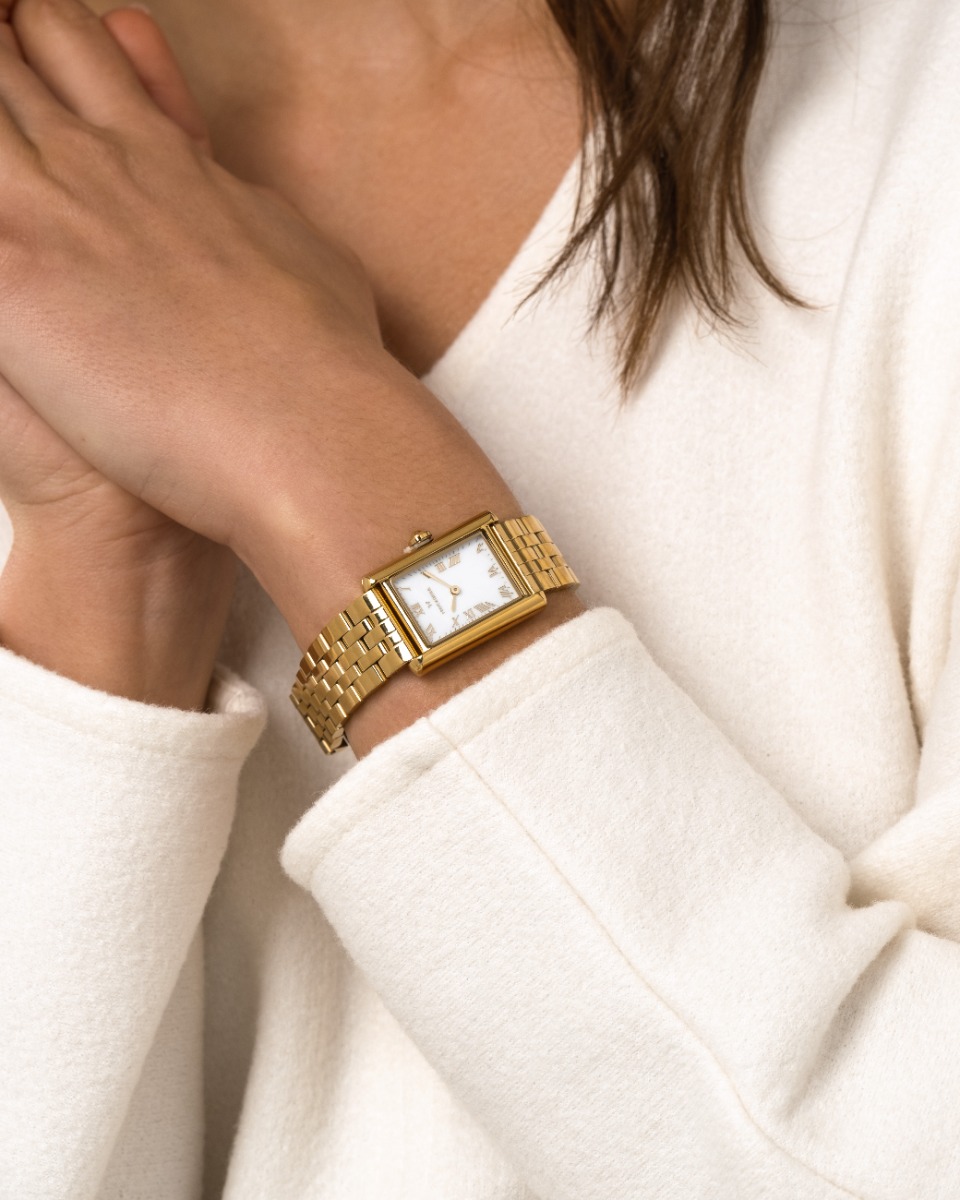 Rektangulær gullfarget armbåndsur med hvit urskive og romertall, festet til lenke i polert metall