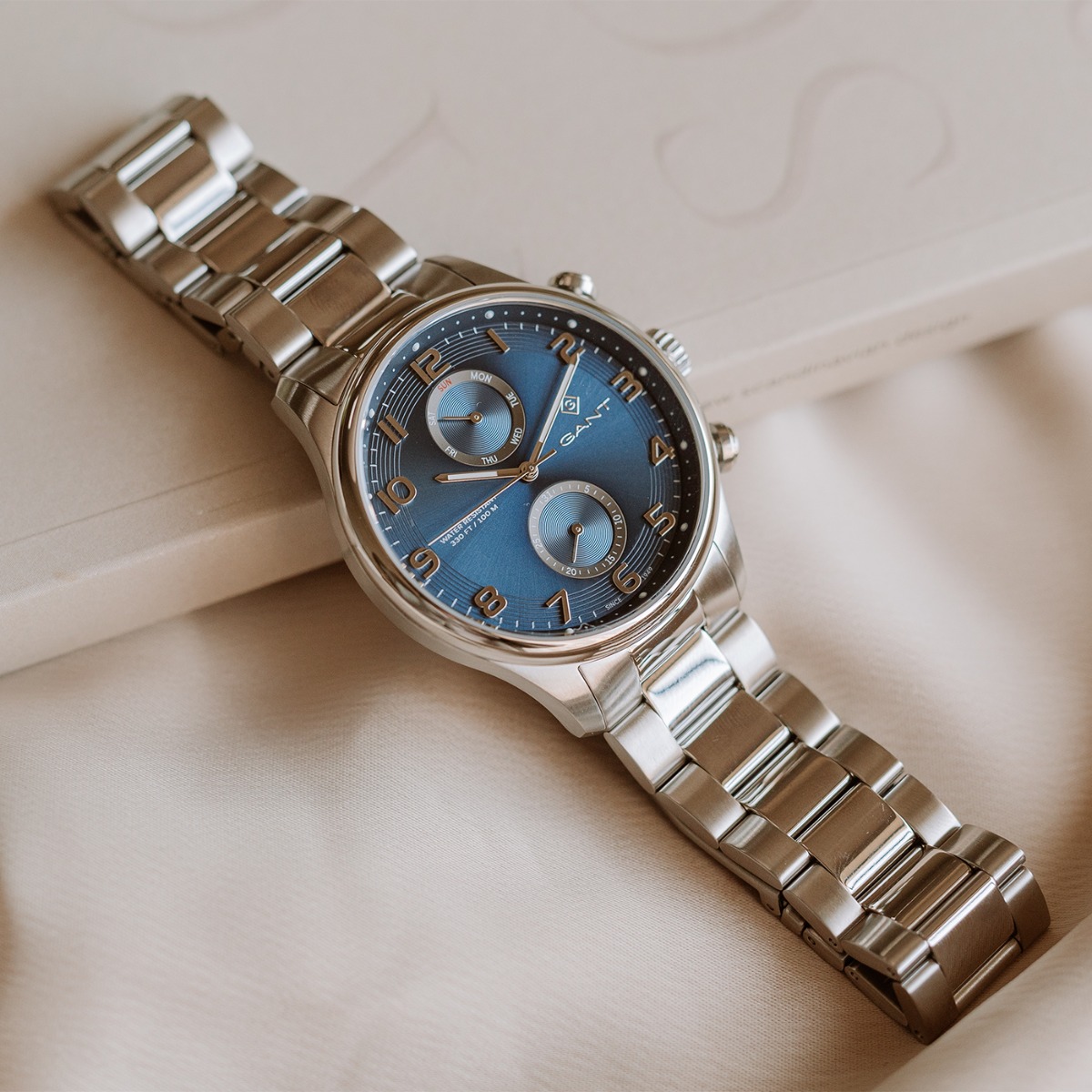 Sølvfarget herreklokke med blå urskive, tre visere og lenkearmbånd, vist forfra på hvit bakgrunn.