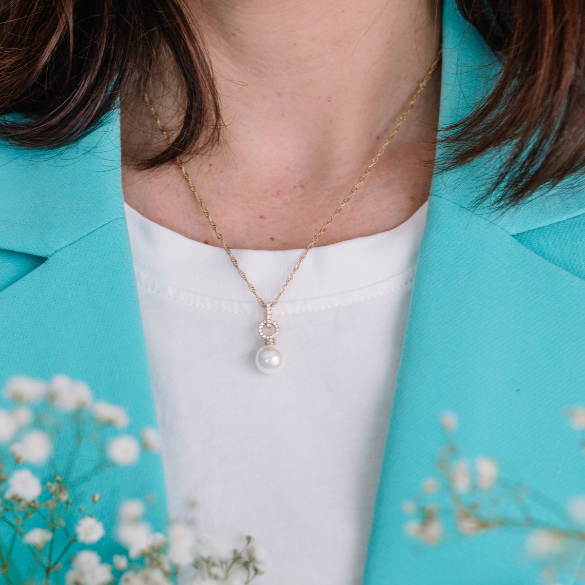 Gullfarget halskjede med vridd kjedeledd og anheng med stor hvit perle festet i en bøyle dekorert med små klare steiner.