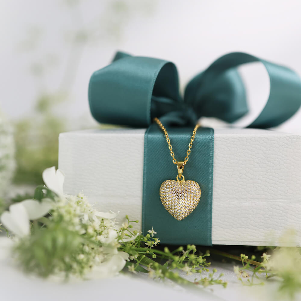 Forgylt halssmykke med gullkjede og hjerteanheng dekket av små glitrende hvite stener.