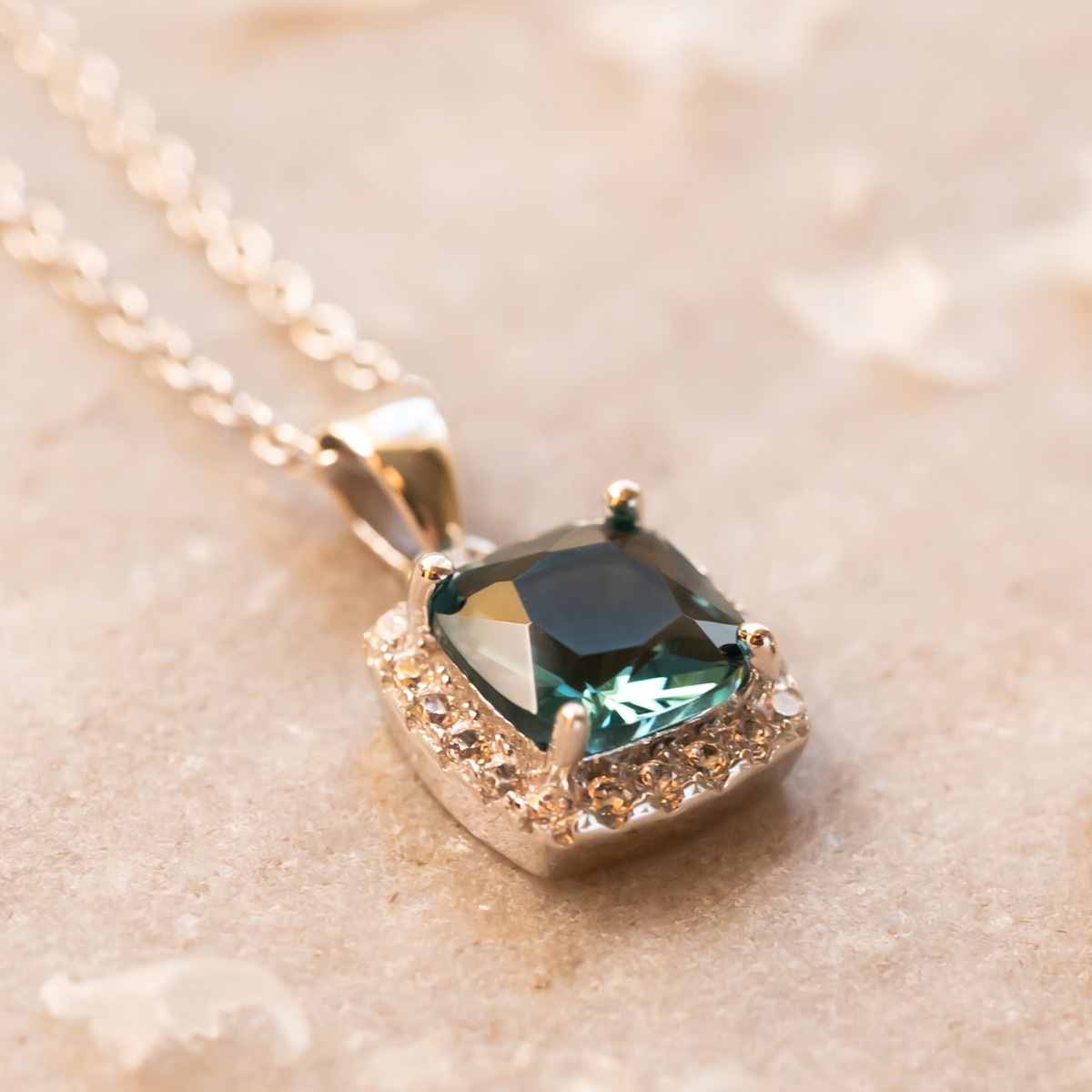 Sølvkjede med firkantet blå stein omgitt av små klare stener i anheng med blank fatning.