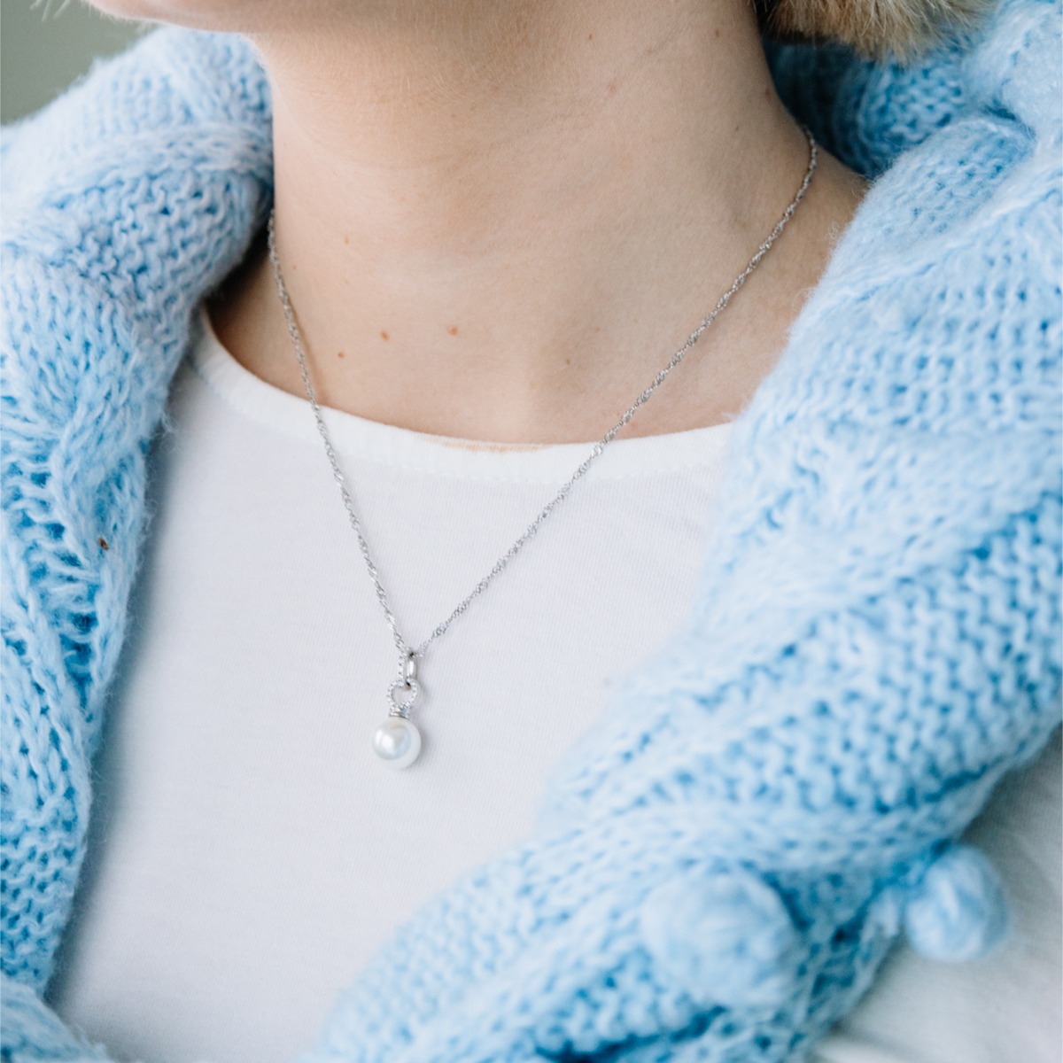 Sølvfarget halskjede med singaporekjede og anheng med hvit rund perle festet i bøyle dekorert med små klare steiner