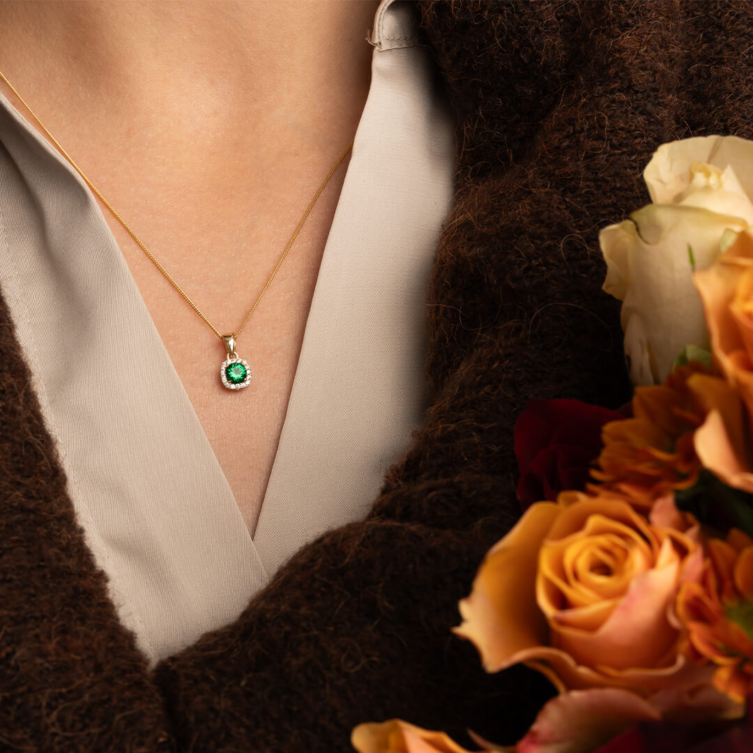 Halskjede i gult gull med firkantet anheng, grønn midtstein og små hvite cubic zirkonia, vist mot hvit bakgrunn.