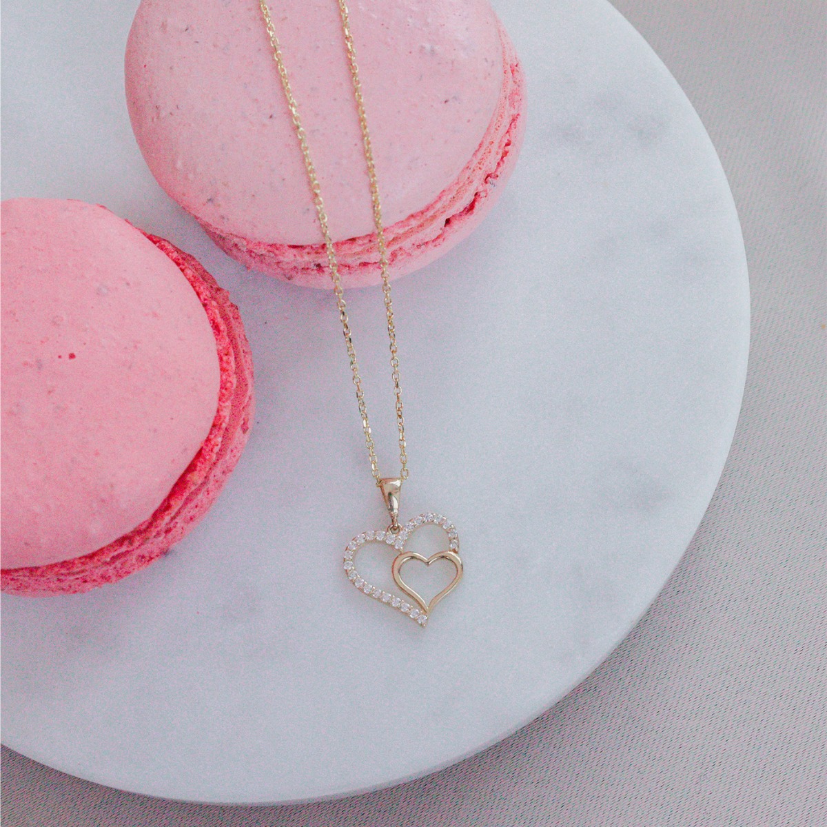 Gullkjede med to sammenflettede hjerteanheng, der det ytre hjertet er dekorert med små, klare stener.