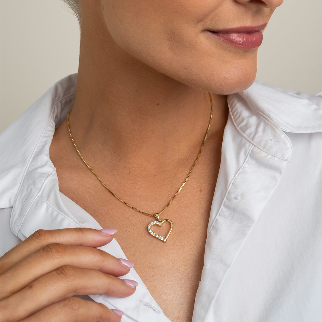 Vakkert halssmykke i gullfarge med hjerteanheng prydet med glitrende hvite stener.