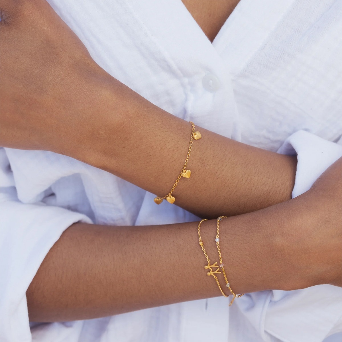 Forgylt armbånd med fem små hjerteformede anheng og justerbar lenke, mot hvit bakgrunn.