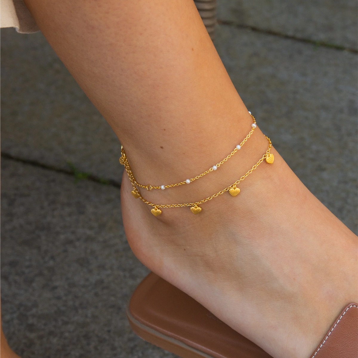 Forgylt armbånd med fem små hjerteformede anheng og justerbar lenke, mot hvit bakgrunn.