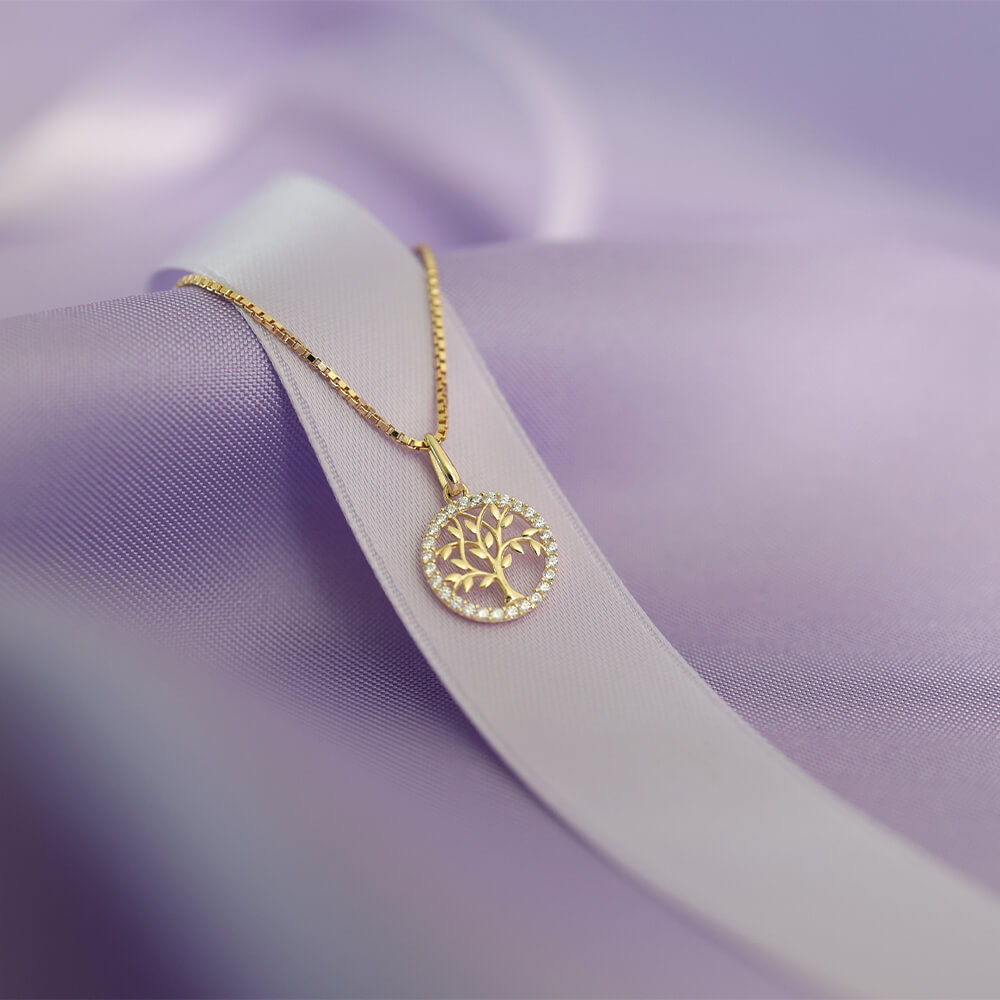 Gullkjede med rundt anheng formet som livets tre, omgitt av små, klare stener i en sirkel rundt motivet."