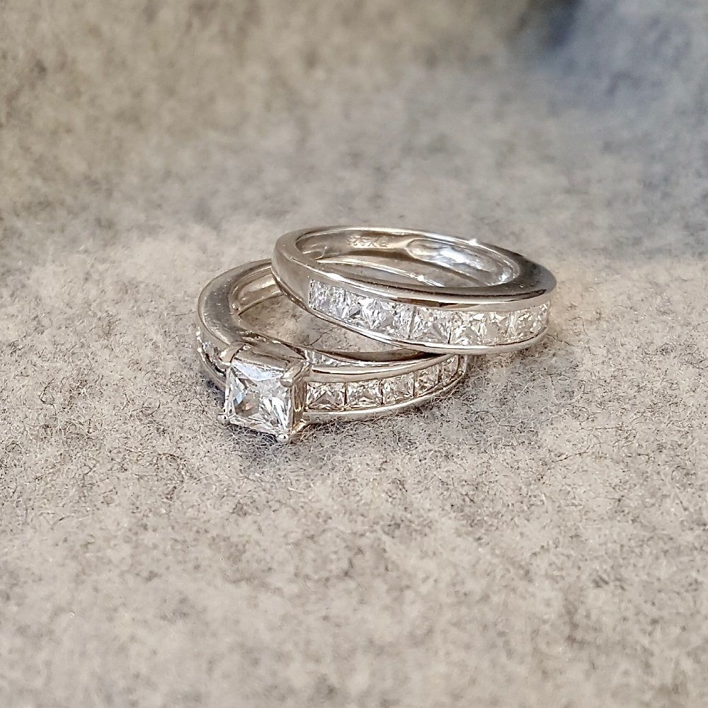 To sølvringer med rektangulære zirkonia-steiner, den ene med forhøyet midtstein i firkantet slip.