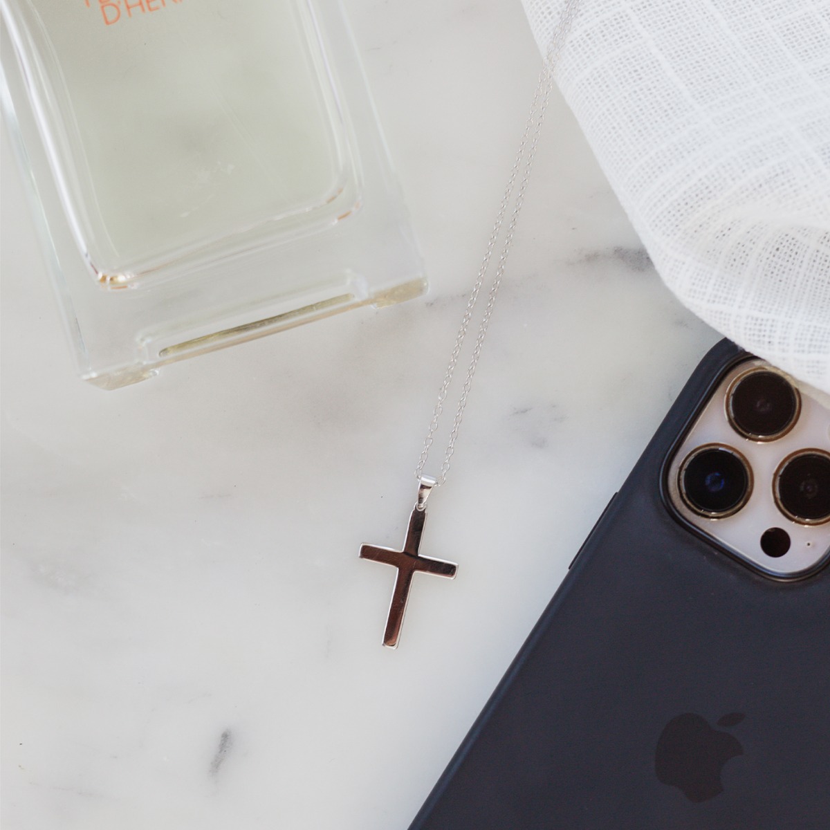 Et halssmykke i sølvfarge med anheng av kors.