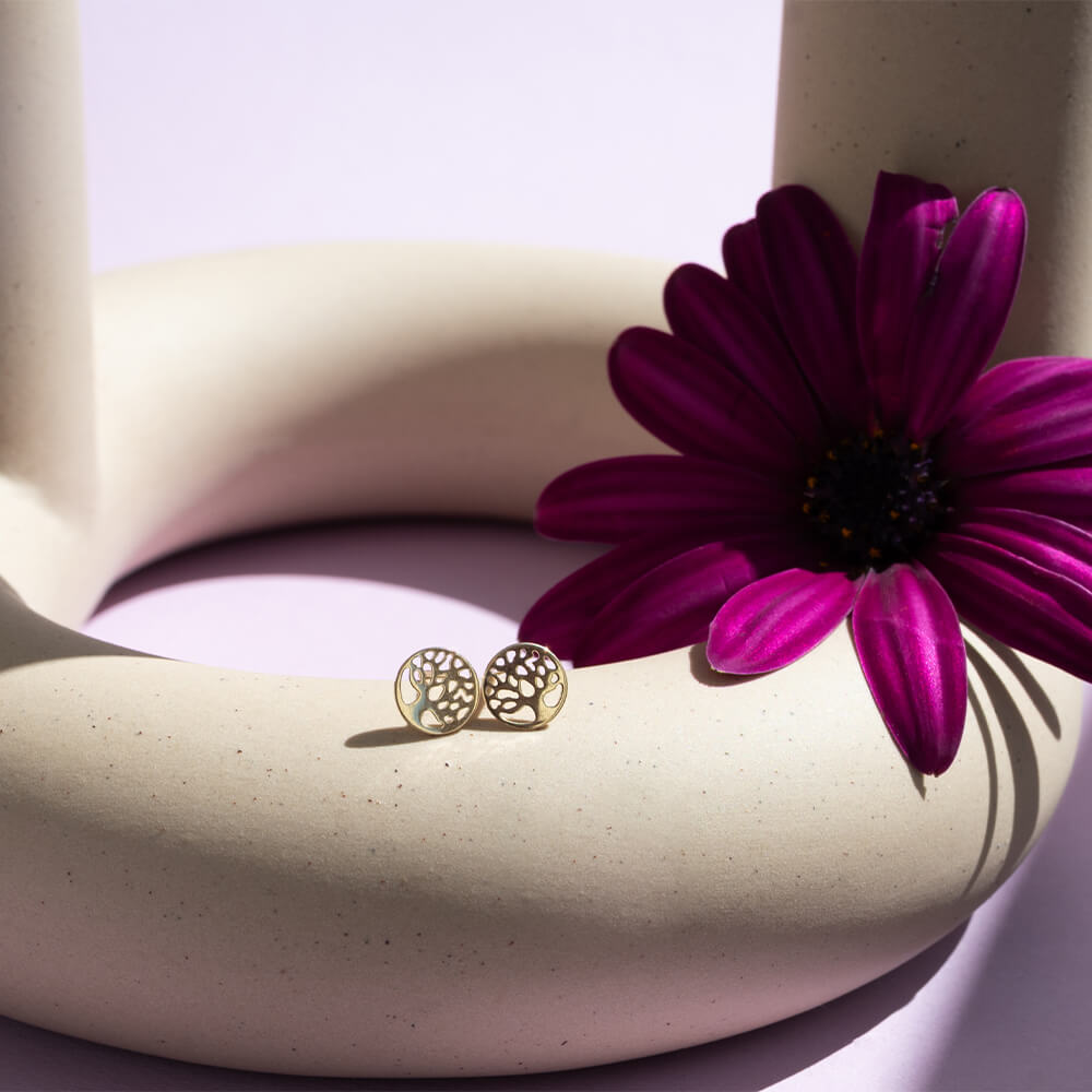 Gylne øredobber i sirkel med utskåret motiv av livets tre, laget i blankpolert gull med glatt overflate.