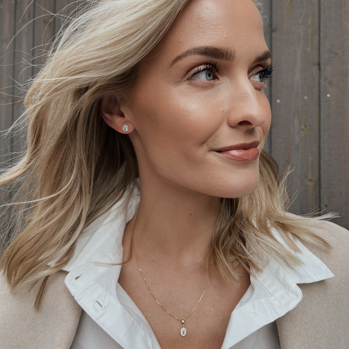 Gullbelagte øredobber med oval klar stein i midten, omgitt av små glitrende zirkonia-steiner.