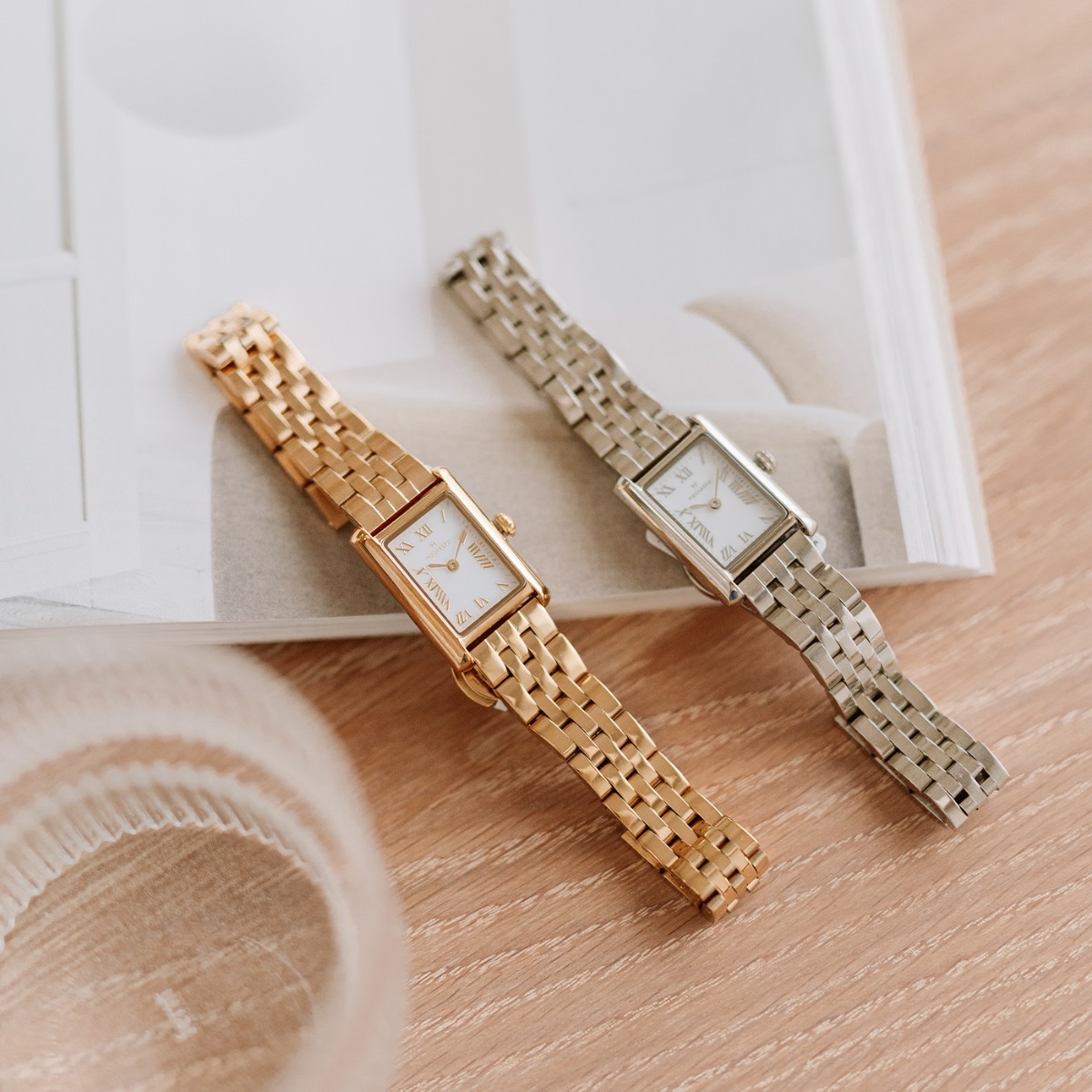 Rektangulær gullfarget armbåndsur med hvit urskive og romertall, vist mot hvit bakgrunn