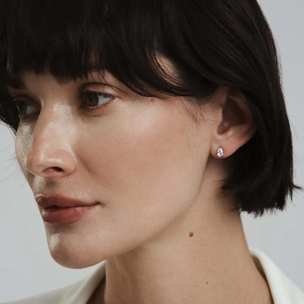 Sølvfarget smykkesett med kjede og to dråpeformede øredobber plassert i en brun eske med filtaktig innside.