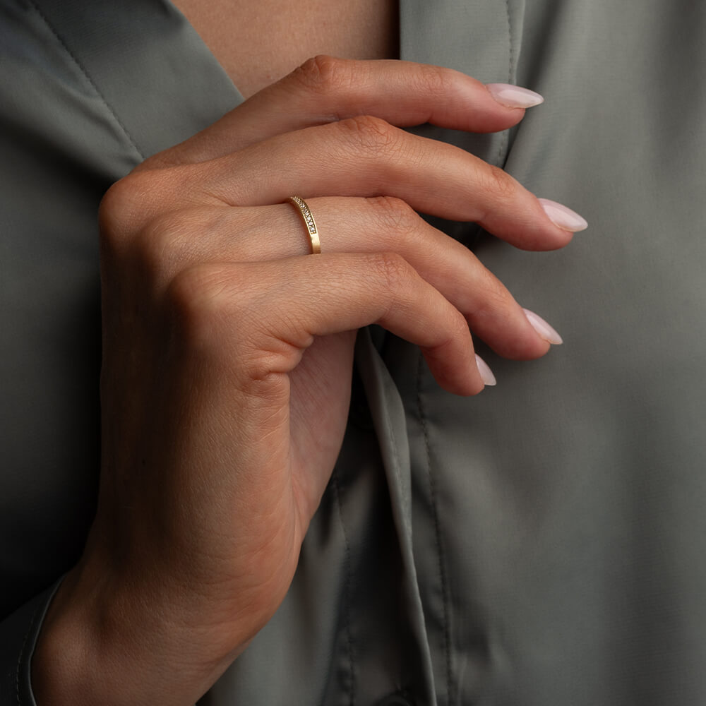 Gullfarget ring med én rad små, klare steiner langs toppen, vist mot hvit bakgrunn med lett skygge under ringen.