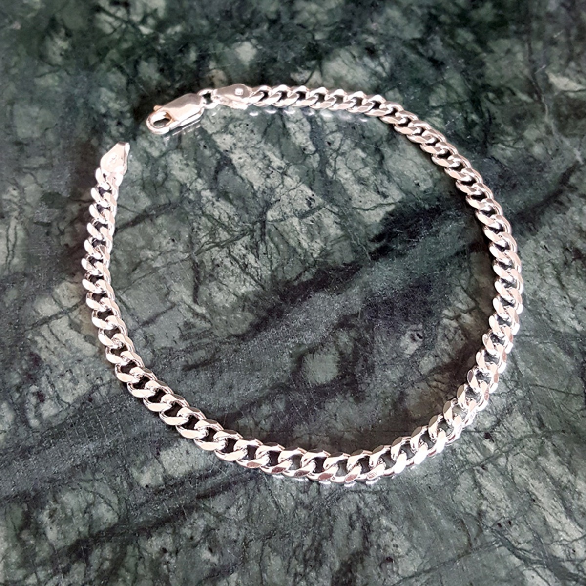 Blankt sølvarmbånd med flate kjedeledd og lås, avbildet mot hvit bakgrunn.