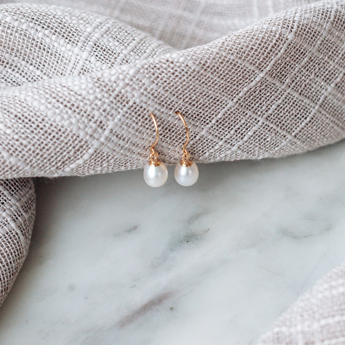 Et par øredobber med perler og bakstykke av hengende krok i gullfarge.