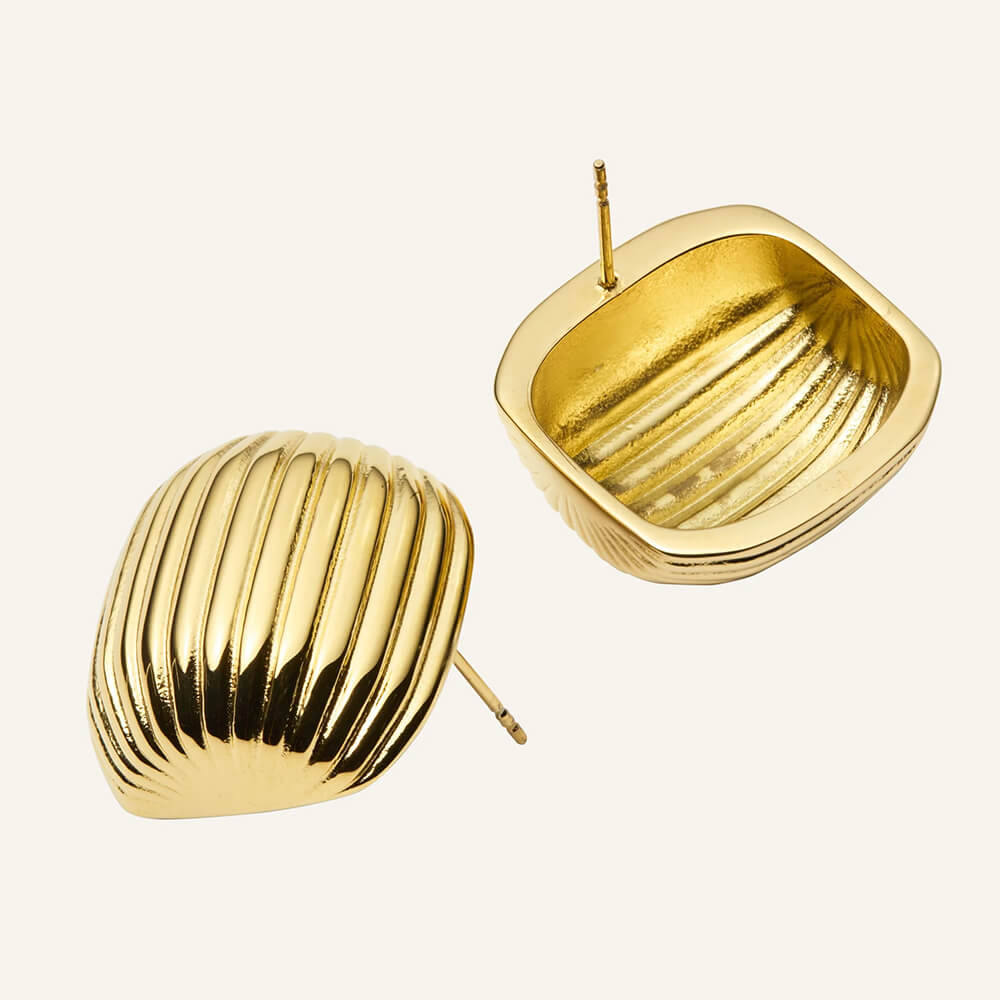 Et par gullfargede øredobber med buet form og jevne horisontale riller, avbildet mot en hvit bakgrunn med lett refleksjon.