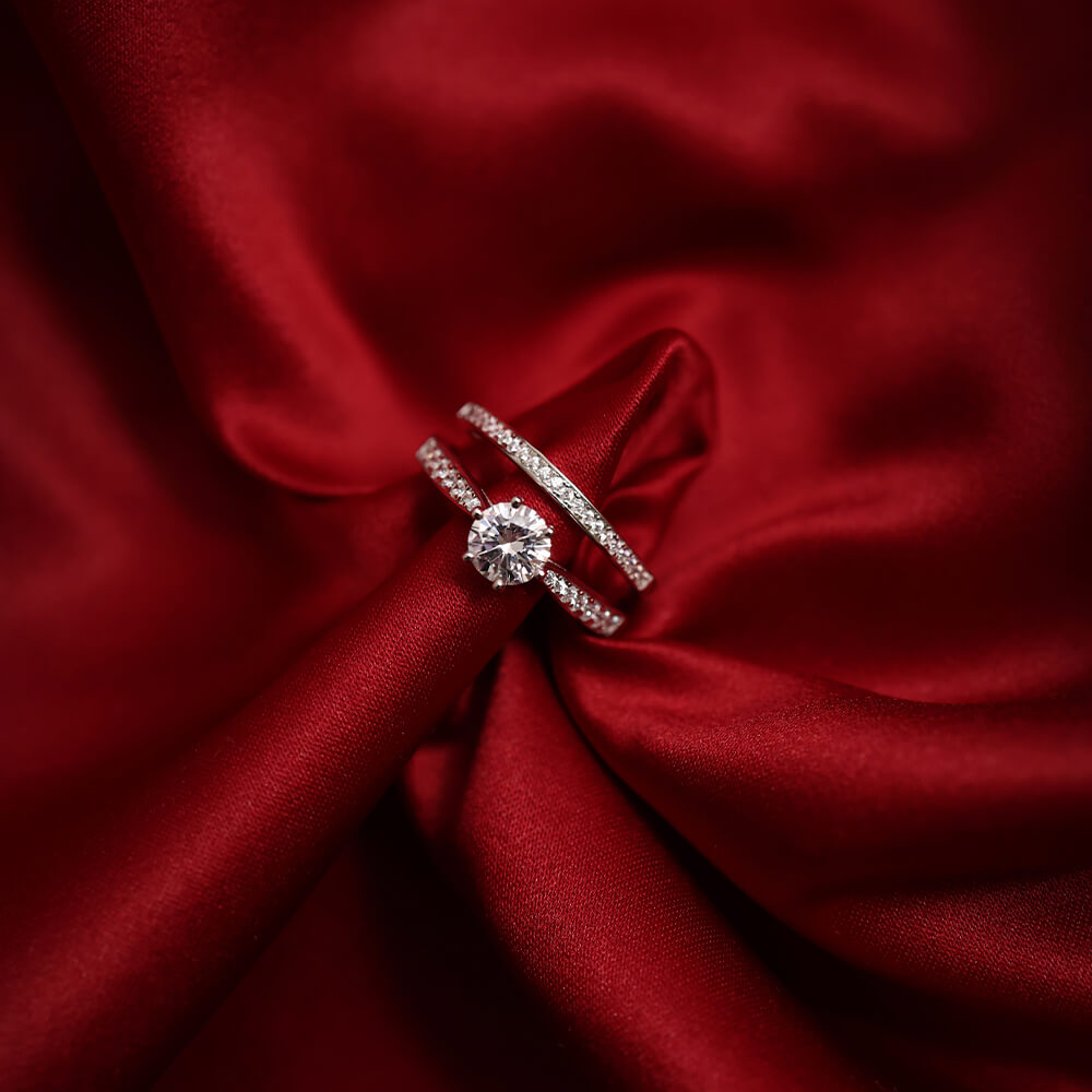 Diamantring i hvitt metall med rund midtsten og pavébesatte sideskinner, fotografert mot hvit bakgrunn.