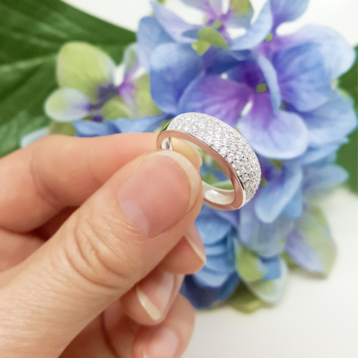 En sølvring med tre rader små diamanter i pavé vist på skrå med uskarp bakgrunn