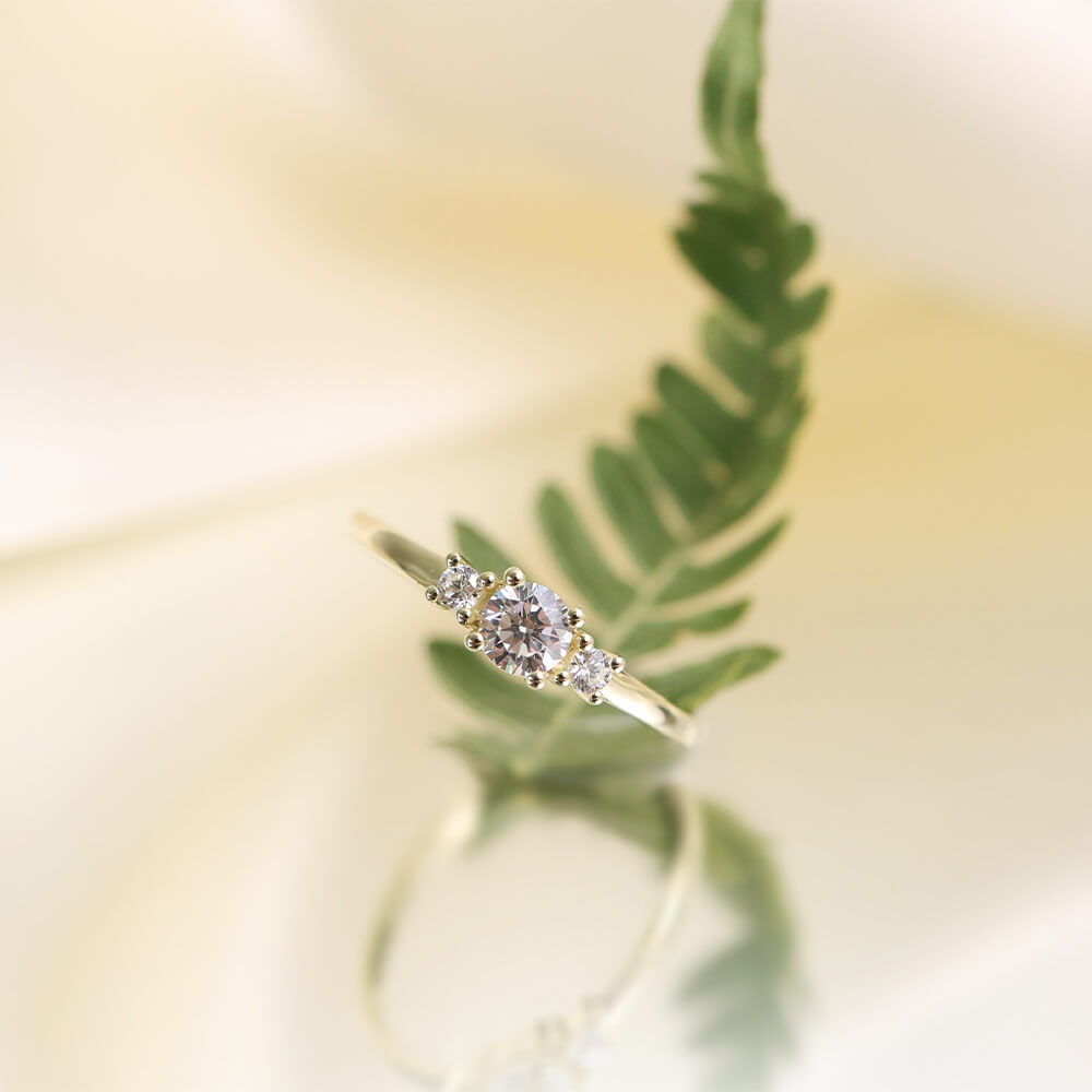 En gullring med tre runde diamanter i kløfatning med størst diamant i midten på hvit bakgrunn