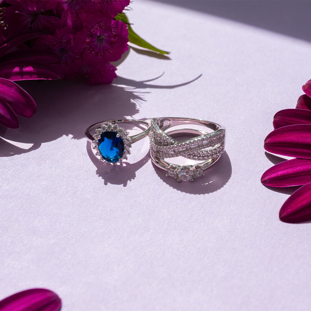 En sølvring avbildet forfra med tre runde, klare steiner på rekke, holdt av små klør på en smal og blank ringskinne mot hvit bakgrunn.