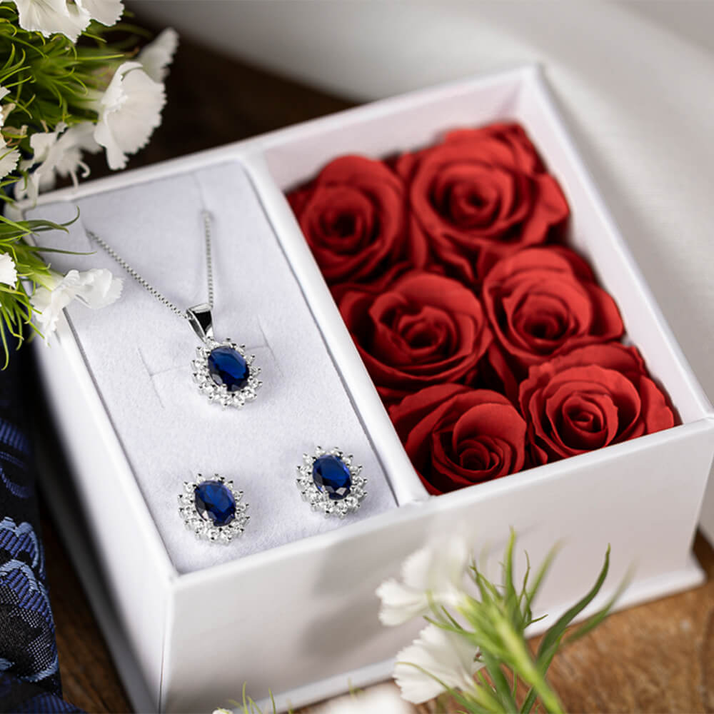 Sølvfargede øredobber med ovale blå stener omgitt av små klare stener, mot hvit bakgrunn.