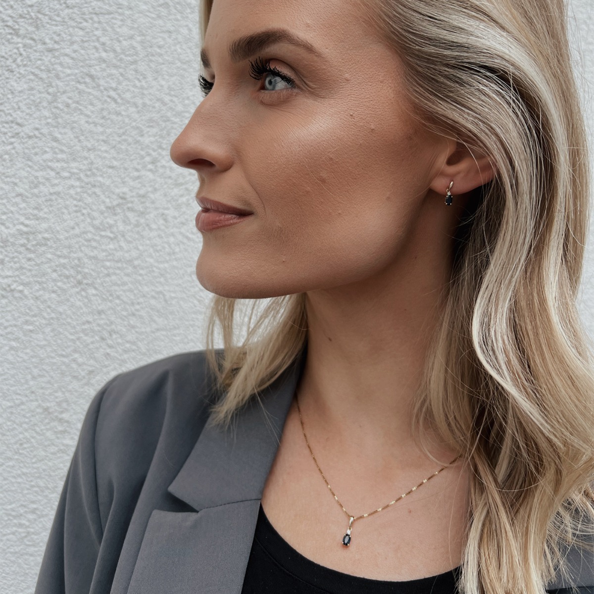 Halskjede i gult gull med anheng som har en oval blå safirsten og en liten klar sten festet over den blå steinen.