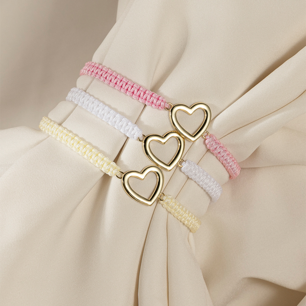 Et Frelsesarmeen vennskapsarmbånd i hvitt med smykke i forgylt sølv på hvit bakgrunn og rød Frelsesarme-logo øverst til venstre.