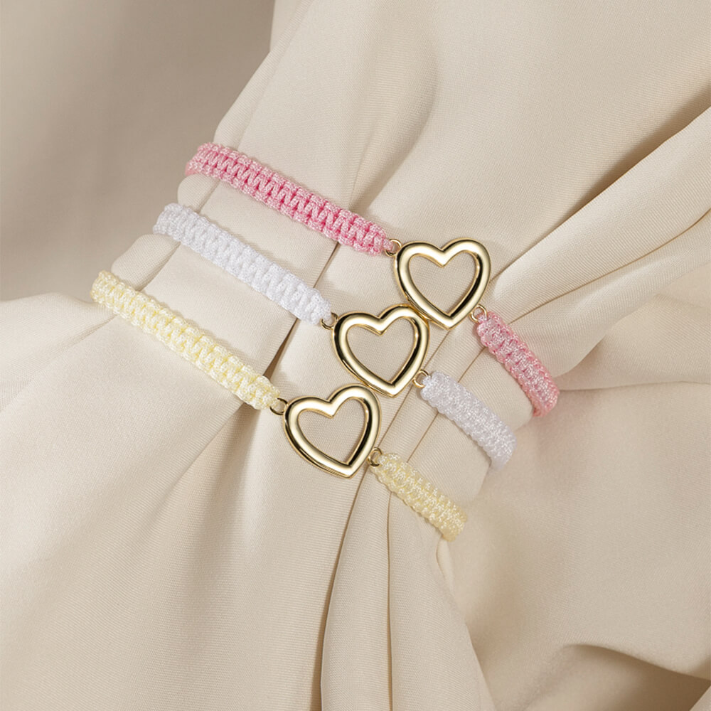 Et Frelsesarmeen vennskapsarmbånd i rosa med hjerte i forgylt sølv på hvit bakgrunn og rød Frelsesarme-logo øverst til venstre.