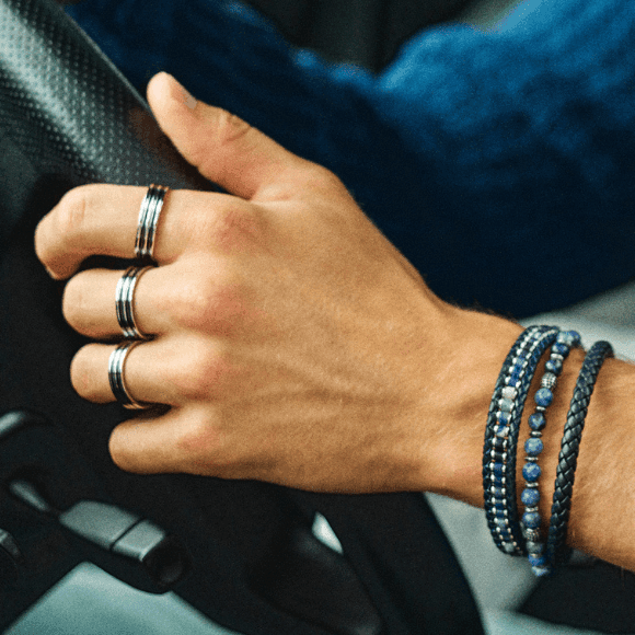 Ringer til menn Nærbilde av hånden til en mann som styrer rattet på en bil. På tre av fingrene har han stilige ringer og flere armbånd på håndleddet.