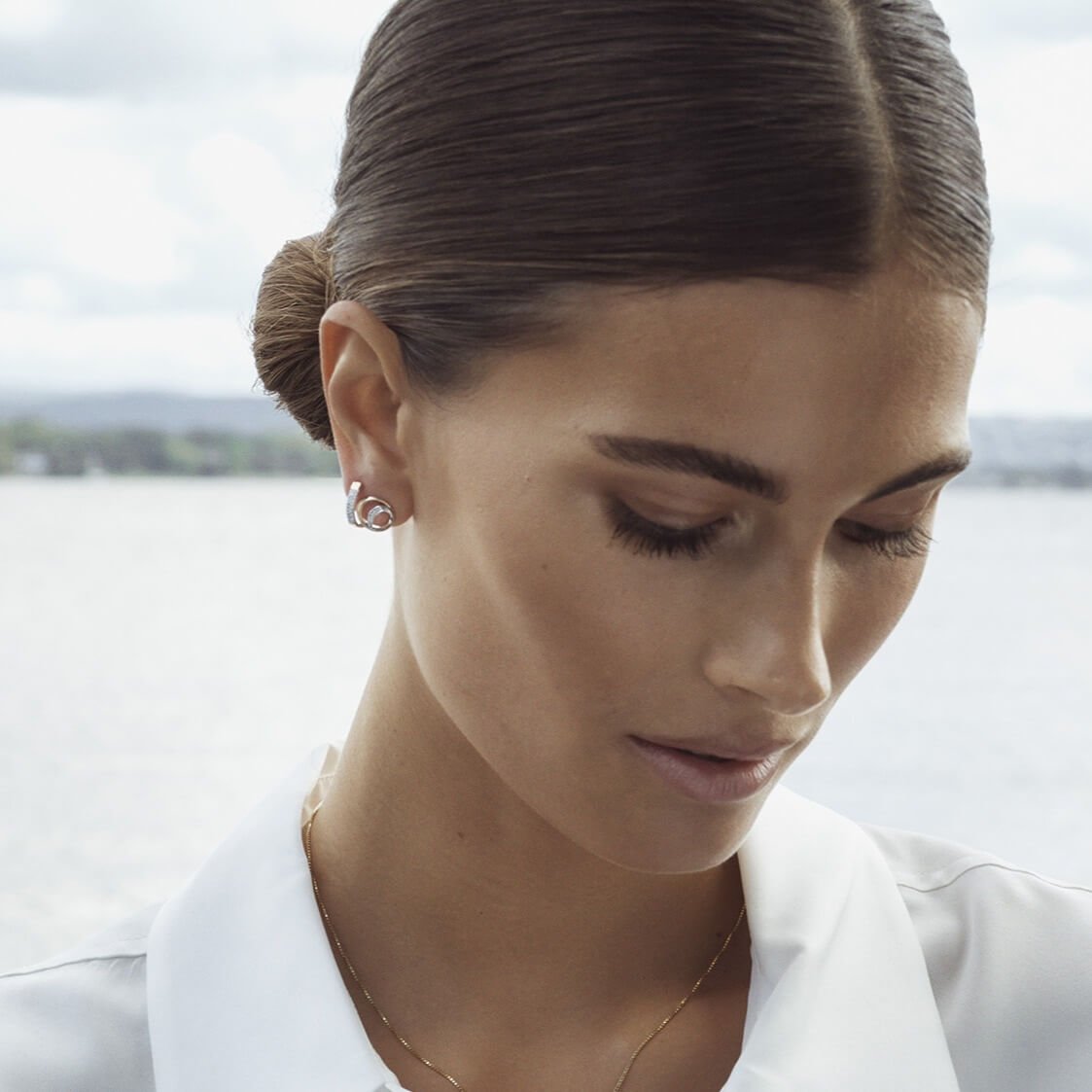 Jente med brunt hår i hestehale og gulløredobber som titter ned