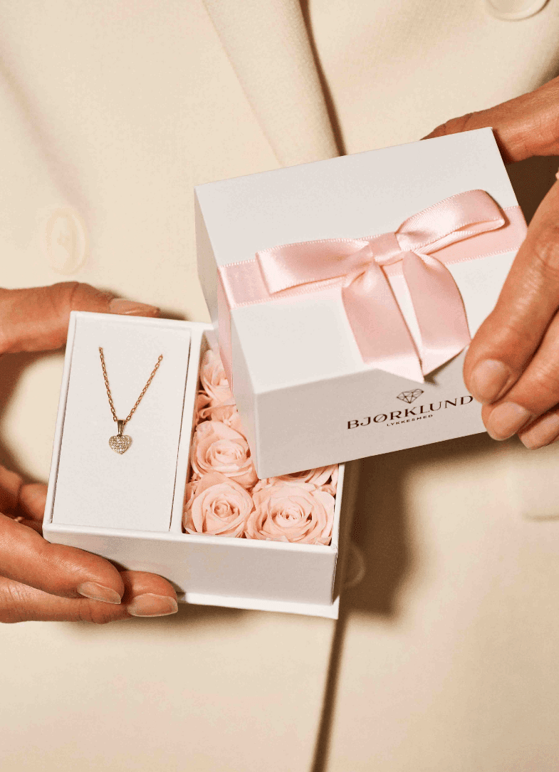 Gi en mer personlig gave! Nærbilde av en gaveeske fra Bjørklund som inneholder et diamantsmykke og mange rosa roser
