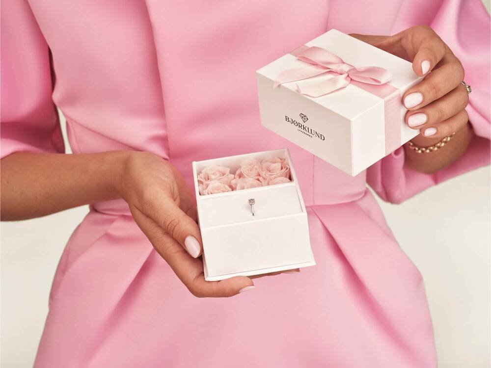 Julegave fra henne En kvinne med rosa kjole holder en hvit gaveeske med rosa bånd på utsiden og rosa roser på innsiden