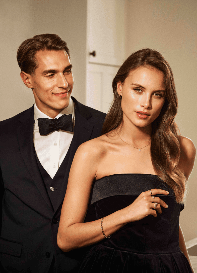 Les mer om hvordan gaver styrker relasjonen! Ungt, vakkert par som har pyntet seg i sort kjole og smoking. Mannen smiler og ser på kvinnen mens kvinnen ser lurt i kamera