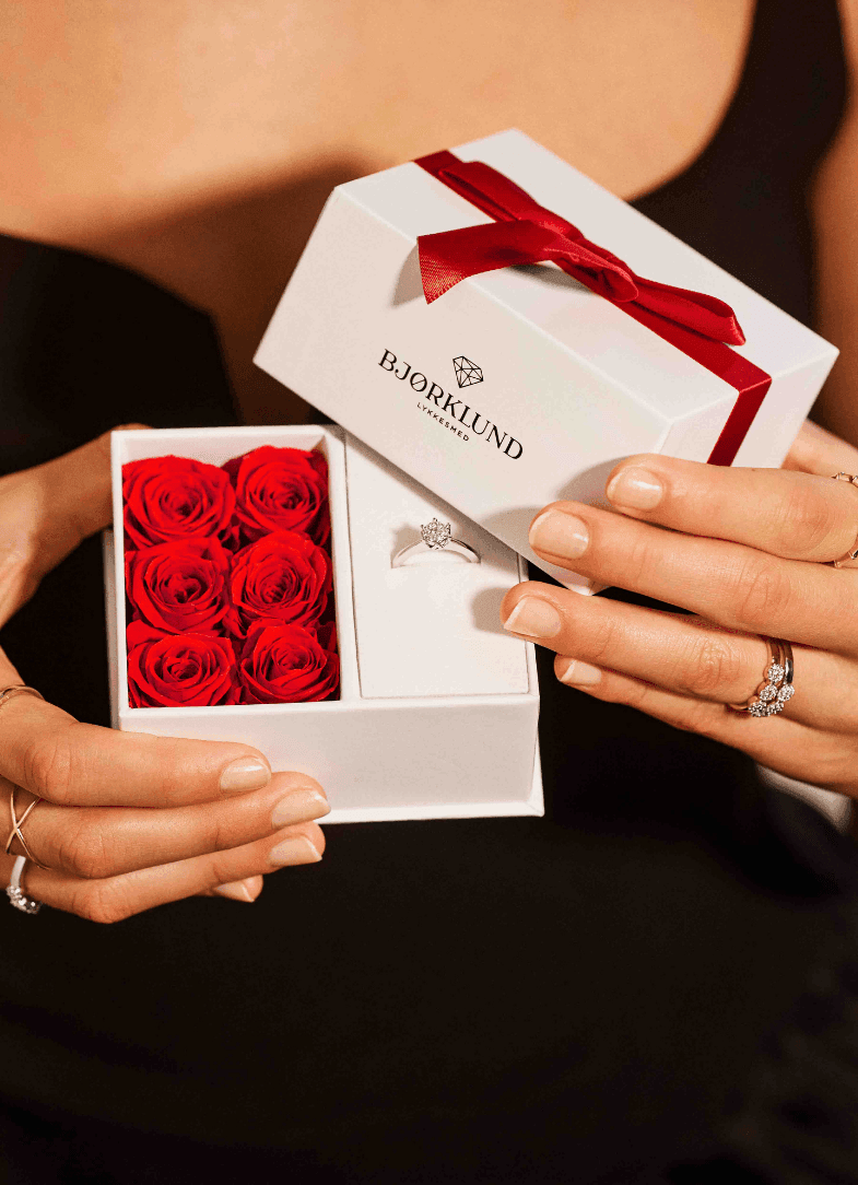 Se vårt univers av gaver! Nærbilde av en gaveeske fra Bjørklund som inneholder en vakker diamantring og mange røde roser