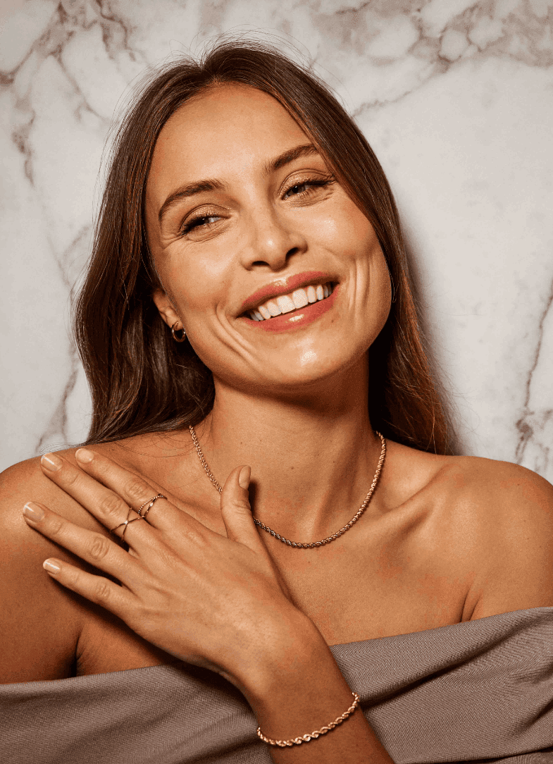 Se ønskeliste Ung kvinne som smiler med tennene og øynene. Hun holder hånden på skulderen og viser frem vakre ringer