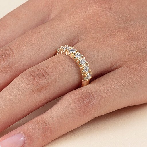 Nærbilde av en kvinnehånd, tett på ringfingeren som har en allianse i gull på seg, med flere diamanter rundt hele ringen.