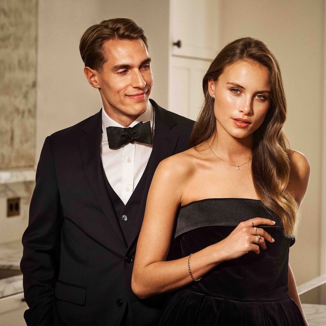 Kjøp din forlovelsesring hos Bjørklund Et ungt, vakkert par i kjole og smoking. Mannen smiler og ser på kvinnen mens