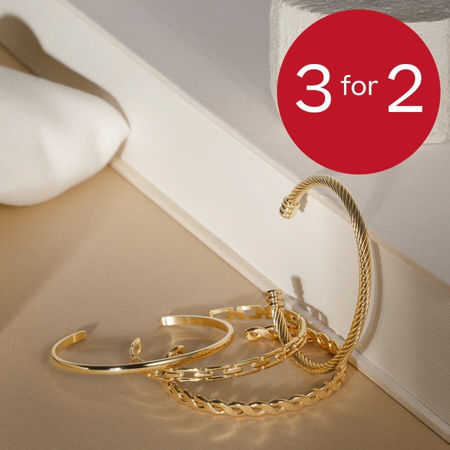 Fire gullfargede armbånd ligger på et lyst bord ved siden av en bok, med en rød sirkel med teksten 3 for 2.