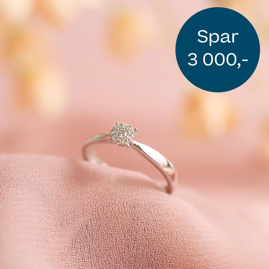 En diamantring i hvitt gull hviler på rosa tekstil. En mørkeblå sirkel øverst til høyre har teksten Spar 3 000,-
