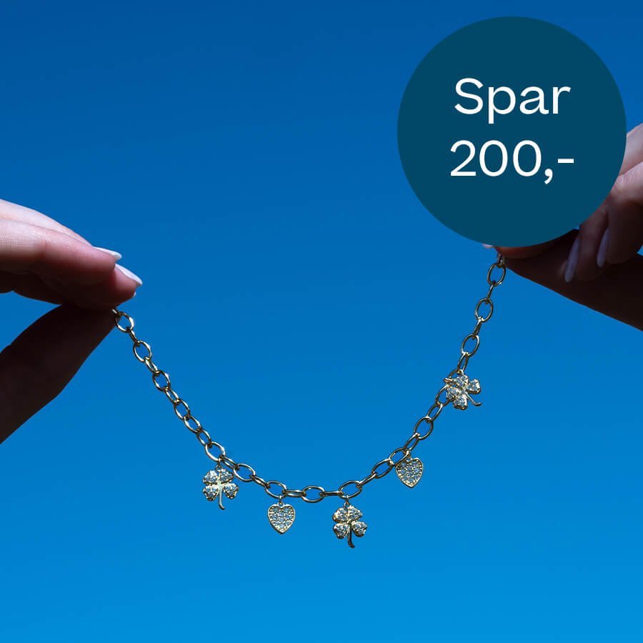 To hender holder et gullfarget charm-armbånd med hjerter og firkløvere mot klar blå himmel, med tilbudssirkel.