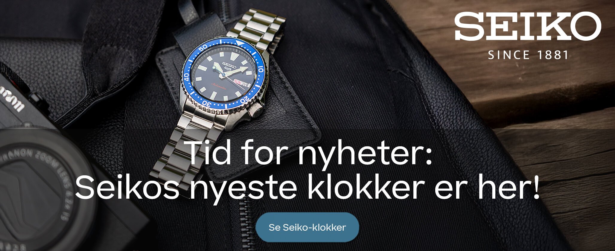 Reklamebilde for Seiko med en klokke med blå bezel og metalllenke, liggende på en svart veske med teksten «Tid for nyheter: Seikos nyeste klokker er her!».